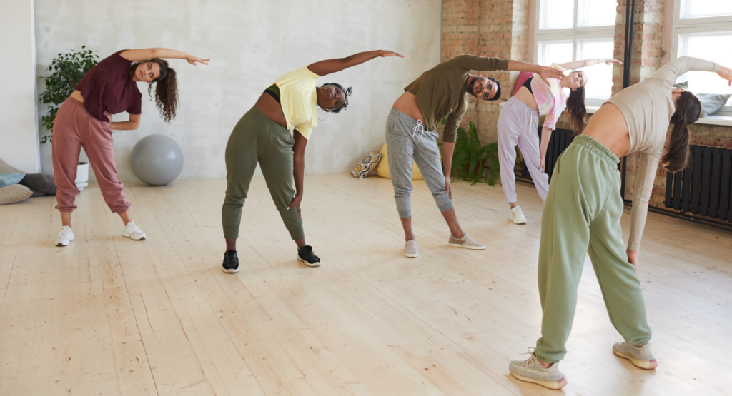 Group of men and women stretching by leaning to one side with their arm extended overhead.