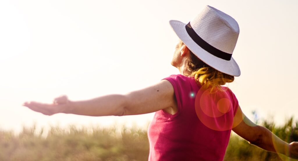 woman standing in the sunshine wearing a red shirt and white hat